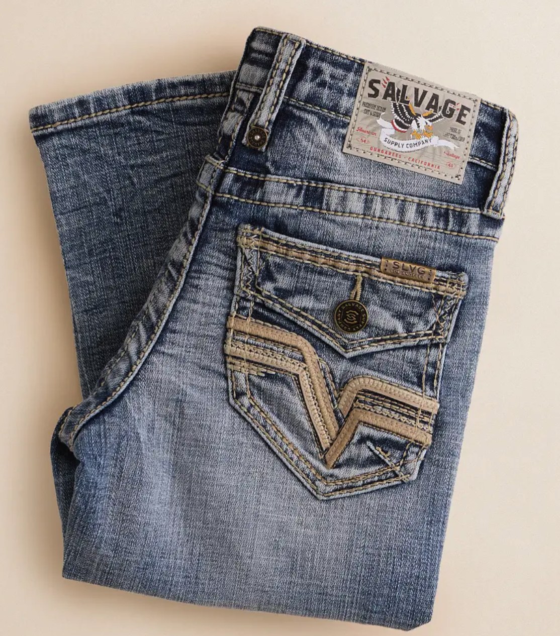 Close-up of dark indigo raw selvedge denim with gold contrast stitching and cuffed hem showing the clean grey selvedge edge